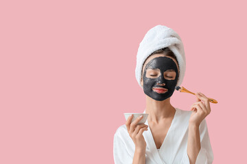 Young woman applying activated charcoal mask on her face against color background