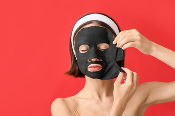 Wall Mural - Young woman with activated charcoal mask on her face against color background