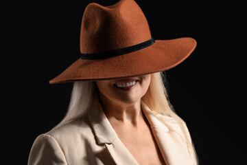 Wall Mural - Smiling mature woman in stylish felt hat on dark background