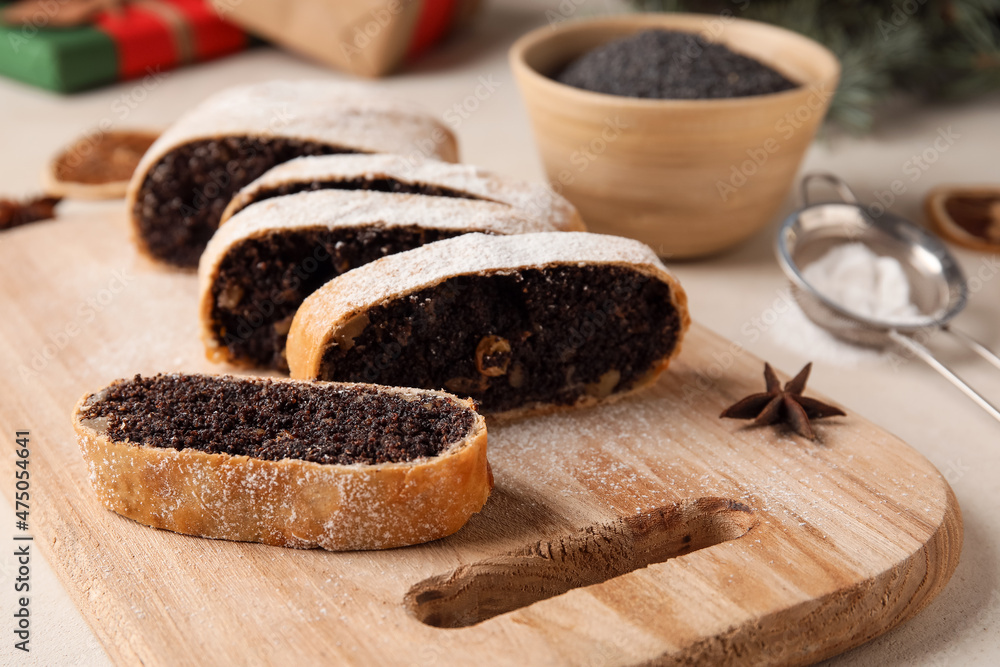 Wooden board with cut poppy seed strudel on light background