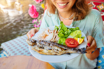 Happy woman holds a plate of freshly baked rainbow trout in a fish restaurant