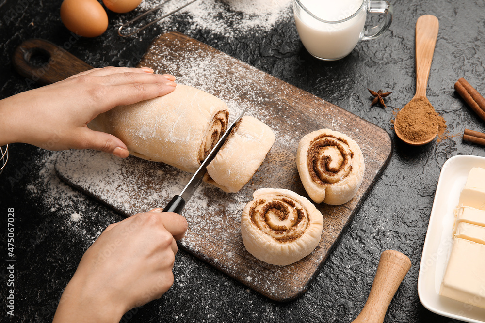 Woman preparing cinnamon rolls on black background