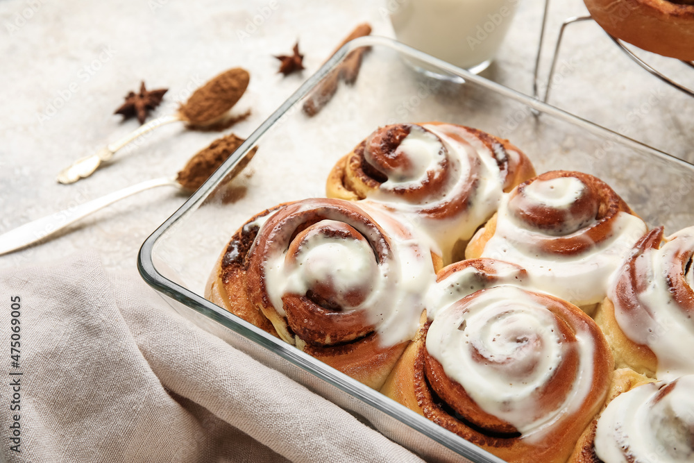Baking dish of tasty cinnamon rolls with cream on light background, closeup