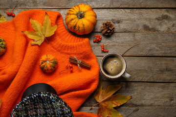 Stylish sweater, hat, cup of coffee and autumn decor on dark wooden background