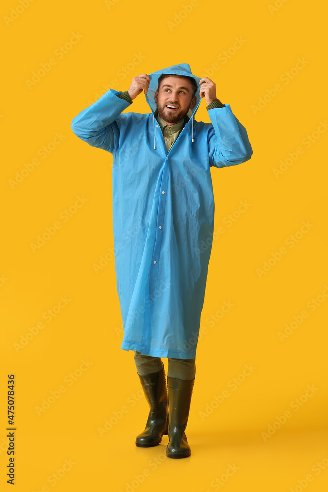 Young man in stylish raincoat on color background