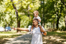 Exploring Nature, Father And Son Are Playing In The Park Father Carries His Son On His Shoulders And They Walk Through The Park One Summer Sunny Day Dressed In The Same Clothes, Dad Point To Something