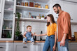 © LIGHTFIELD STUDIOS - Happy parents looking at amazed son sitting on kitchen worktop