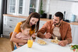 © LIGHTFIELD STUDIOS - Smiling woman feeding pasta to son near husband and orange juice in kitchen