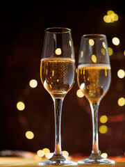 Wall Mural - Two glasses of champagne toast on a dark background with a side garland