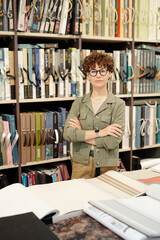 Sticker - Young brunette female shop assistant or manager of studio of interior design looking at you while working with samples of new wallpapers