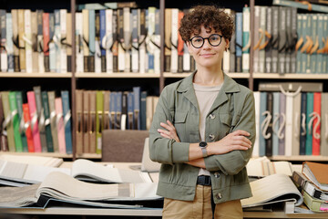 Sticker - Young confident brunette female shop assistant or manager of interior design studio looking at you while working with new samples