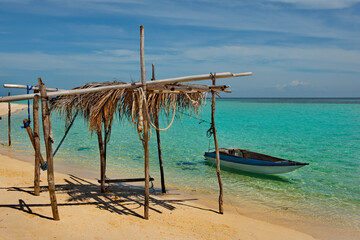 Wall Mural - Malaysia. A palm leaf canopy with a moored boat on the sandy shore of a reef island along the east coast of Borneo.