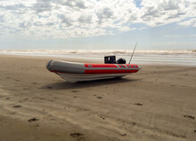 Rigid Hull Inflatable Boat With Outboard Motor In The Shore Beaten By The Waves. Used To Fish At Sea