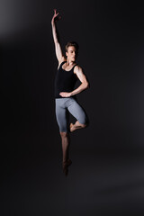 Wall Mural - young and graceful dancer gesturing while performing ballet dance while jumping on black