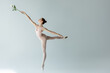 full length of graceful ballerina in bodysuit holding rose and dancing on grey