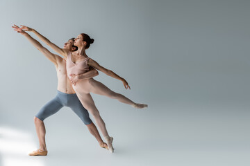 Wall Mural - full length of shirtless man and sensual woman with outstretched hands performing ballet dance on grey