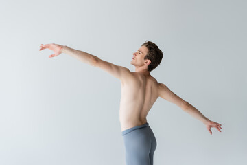 Wall Mural - shirtless young man with outstretched hands performing ballet dance isolated on grey