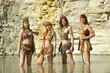 Four girls are dressed as Neanderthal warriors. They are 
covered with mud, filth and dirt and are seen standing 
together in a pond in a stone quarry.
