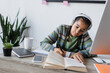© LIGHTFIELD STUDIOS - african american girl in headphones writing near book and computer while studying at home