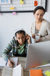 © LIGHTFIELD STUDIOS - african american girl in headphones writing in notebook near computer and mother with tea cup