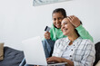 © LIGHTFIELD STUDIOS - excited african american teen girl with closed eyes girl holding credit card near smiling mom and laptop