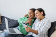 © LIGHTFIELD STUDIOS - smiling african american woman holding credit card near laptop and excited daughter