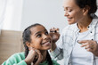 © LIGHTFIELD STUDIOS - african american woman applying mascara on eyelashes of teenage daughter
