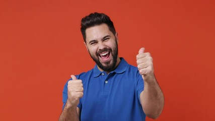 Wall Mural - Cheerful confident young bearded brunet man 20s years old wears blue t-shirt point show thumb up like gesture camera on you motivating encourage isolated on plain red orange background studio portrait