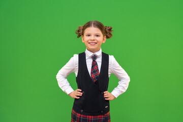 Wall Mural - a schoolgirl in a school uniform put her hands on her sides. a girl with pigtails on a green background.