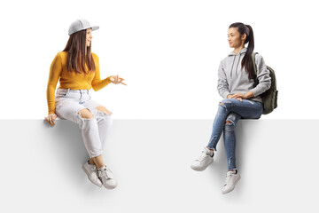 Canvas Print - Two female students sitting on a blank panel and having a conversation