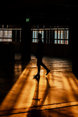 Poster - Vertical shot of the silhouette of a man in a dark studio with sunset lights coming from the window