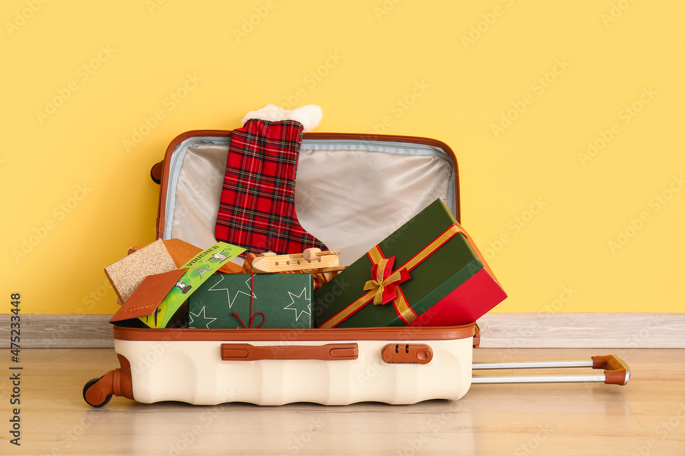 Suitcase, gift boxes, sock and documents near color wall. Christmas vacation concept