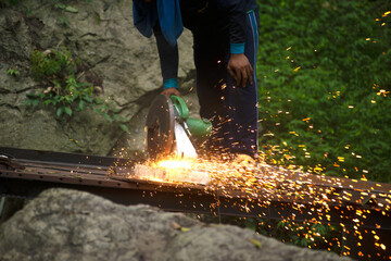 Professional Asian male artisans are cutting metal with a rotating diamond blade. To build an outdoor bridge in the forest.