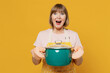 © ViDi Studio - Excited happy elderly housekeeper housewife woman 50s in orange apron hold green saucepan with soup look camera isolated plain on yellow background studio portrait. People household lifestyle concept.