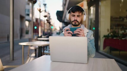 Sticker - Young hispanic man playing video game sitting on table at coffee shop terrace