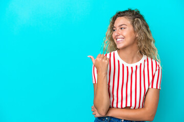 Wall Mural - Girl with curly hair isolated on blue background pointing to the side to present a product