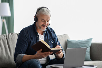 Happy old man having online class, using laptop and headset