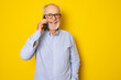 © Danko - Portrait of happy european senior man talking on phone and smiling isolated over yellow background.
