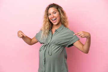 Wall Mural - Girl with curly hair isolated on pink background pregnant and pointing to the belly