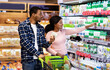 © Prostock-studio - Young black couple with trolley full of products choosing diary products at huge supermarket