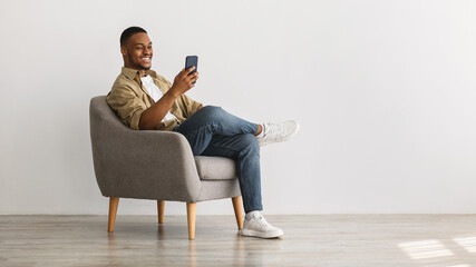 Wall Mural - Cheerful African American Guy Using Mobile Phone Over Gray Background