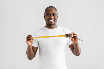 Happy african american handyman or builder in white t-shirt holding tape-line measure and smiling at camera