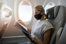 Woman Wearing Face Mask And Reading Book In Airplane. Travel In The Pandemic