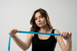 © Volodymyr_sh - Brunette woman with slim body in black top on a diet looking in a camer and showing a blue centimeter tape. Healthy lifestyles concept. Sport and diet.