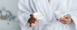 © LIGHTFIELD STUDIOS - partial view of african american woman in bathrobe holding container with face cream in bathroom banner