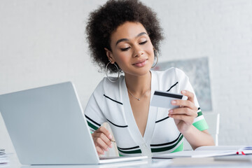 Wall Mural - happy african american woman holding credit card near laptop