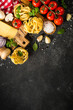 Pasta ingredients on black background. Italian food background. Pasta, parmesan, fresh tomatoes and basil with spices. Top view with copy space.