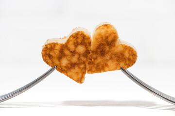 two pancakes in the shape of heart on the forks on white background