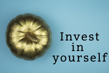 Poster - Top view of golden pumpkin with Invest in yourself text isolated on blue backgroun