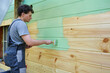 man in a worker's suit is painting the wooden surface of the wall green.